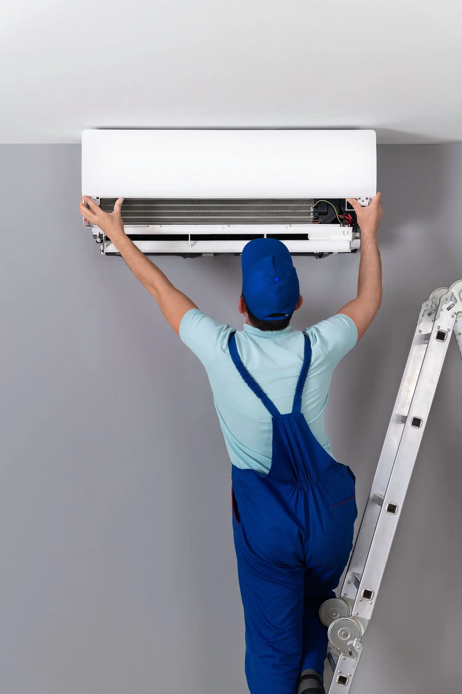 A man in overalls fixing an air conditioner.